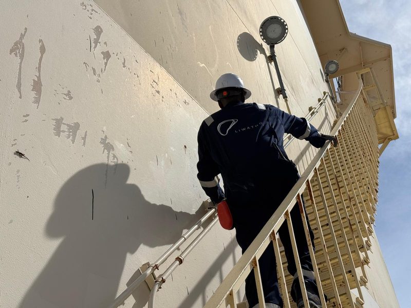 A Liwathon B.O.S. operator in overalls and a hard hat climbs the stairway of a storage tank.