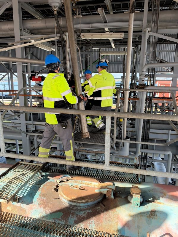 Three Liwathon E.O.S. operators in hard hats and branded high-visibility jackets work together on a rail loading platform.