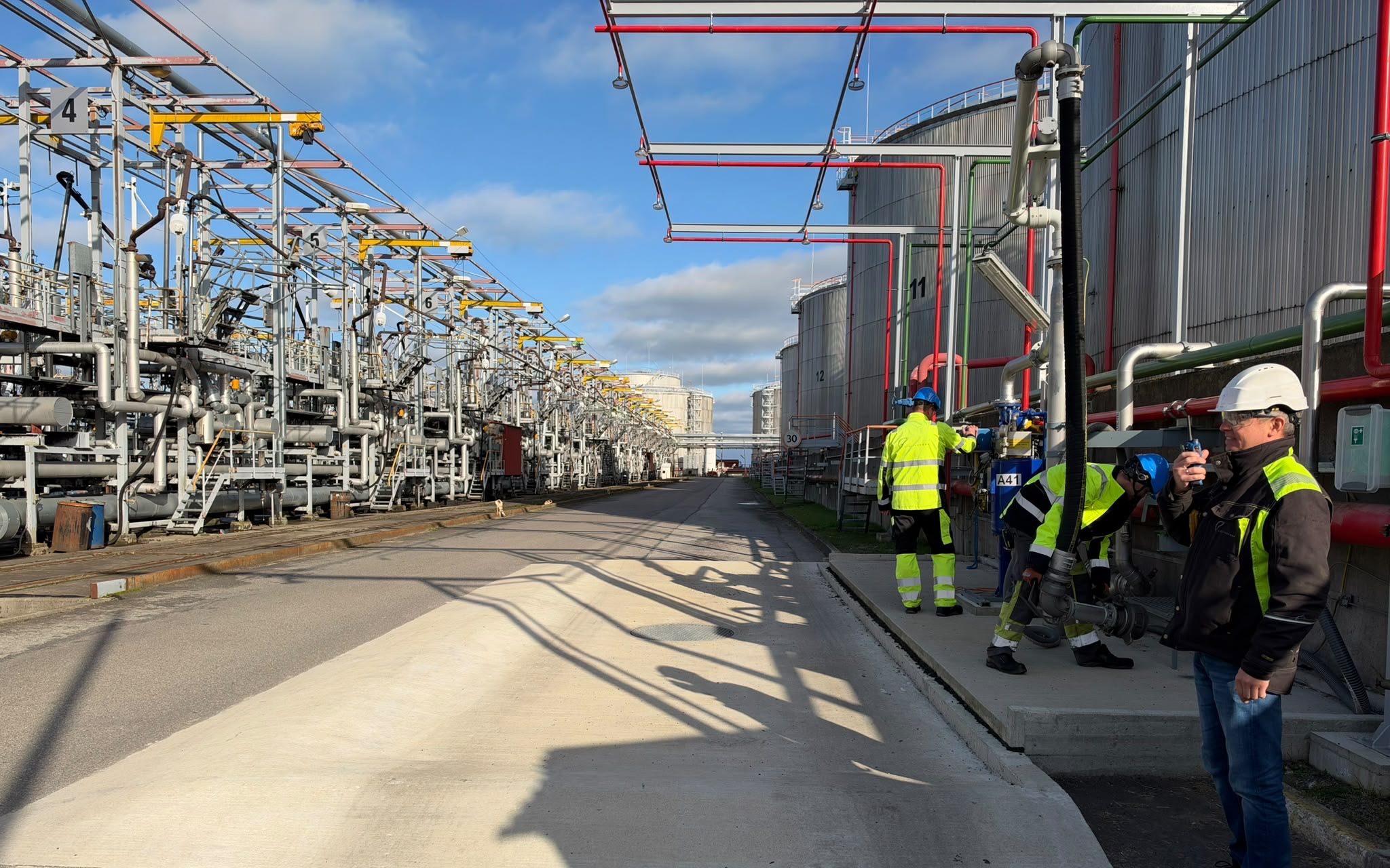 Liwathon E.O.S. operators in high-visibility gear at the truck loading gantry, with storage tanks behind, in Estonia.