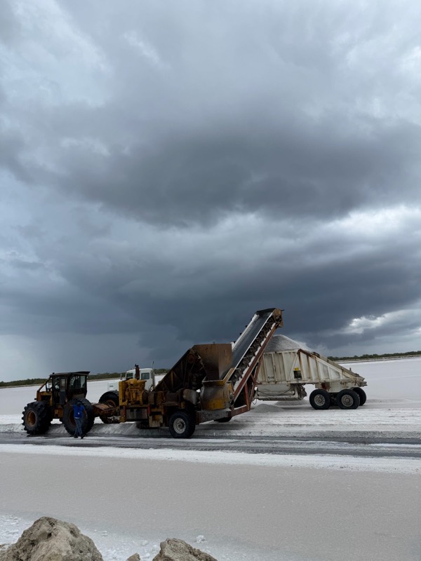 A crew member stands by the harvester on a crystalliser bed under a storm sky.