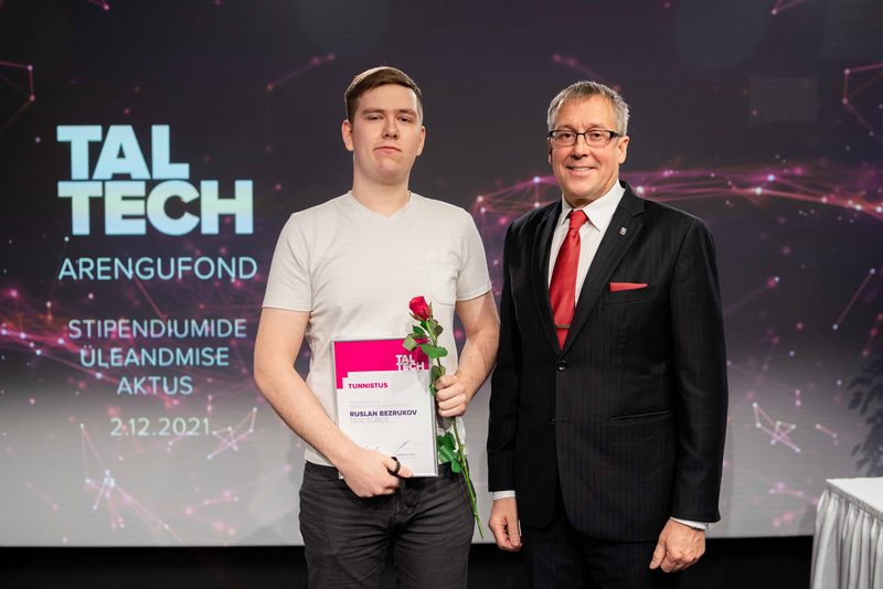 At the TalTech Development Fund (Arengufond) scholarship ceremony on 2 December 2021, the student holds his certificate and a rose beside a man in a suit.