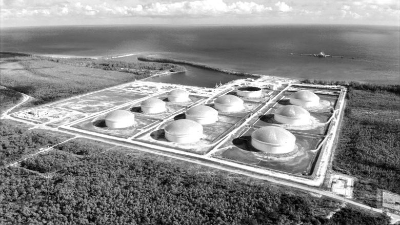 Aerial view of the South Riding Point tank farm on Grand Bahama: domed tanks in their bunds, surrounded by pine forest, with the sea beyond.